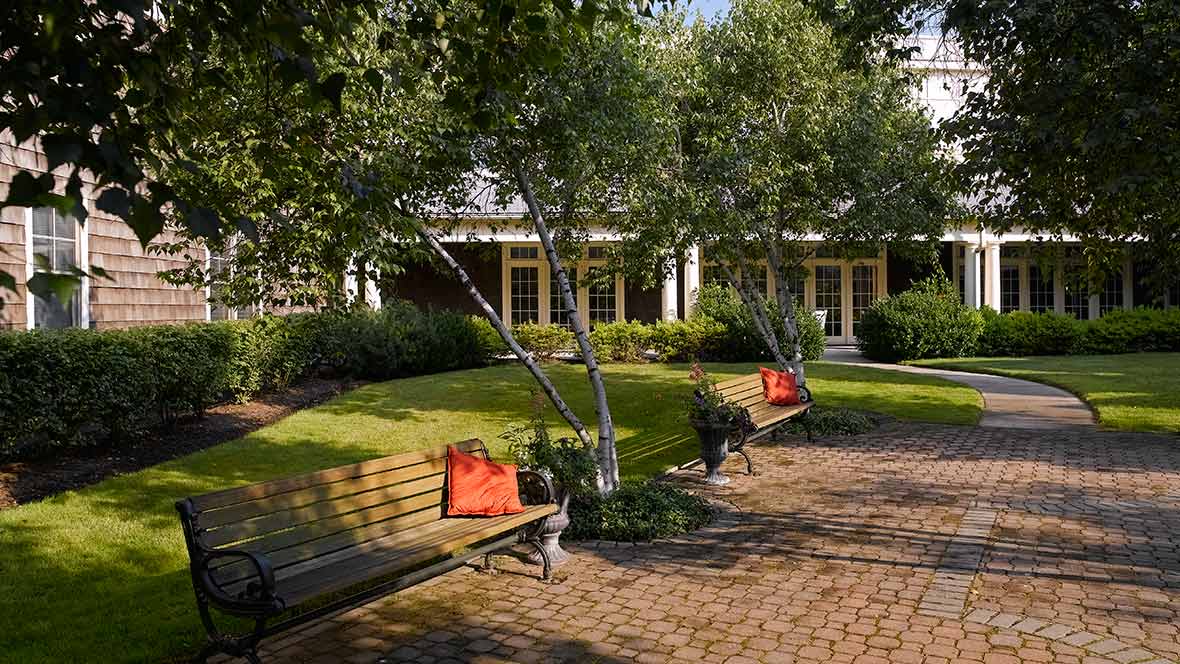 A serene garden scene with benches and a brick pathway surrounded by lush greenery.