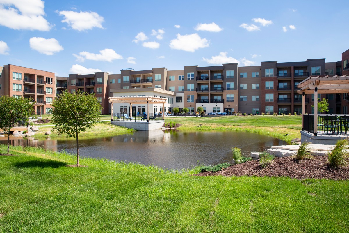 A modern apartment complex with a scenic pond and lush greenery.