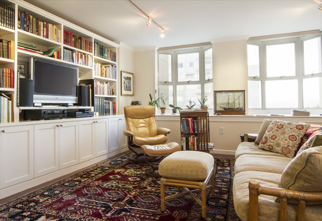 A cozy living room featuring a large bookshelf, television, and comfortable armchair with footstool.