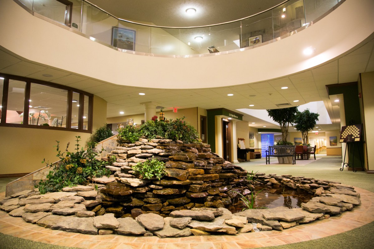 A spacious atrium with a decorative stone water feature and lush plants.