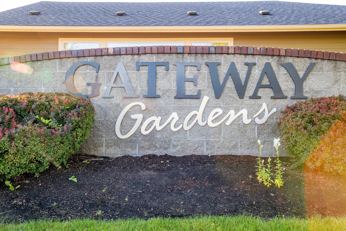 A stone sign for Gateway Gardens with bushes in front.