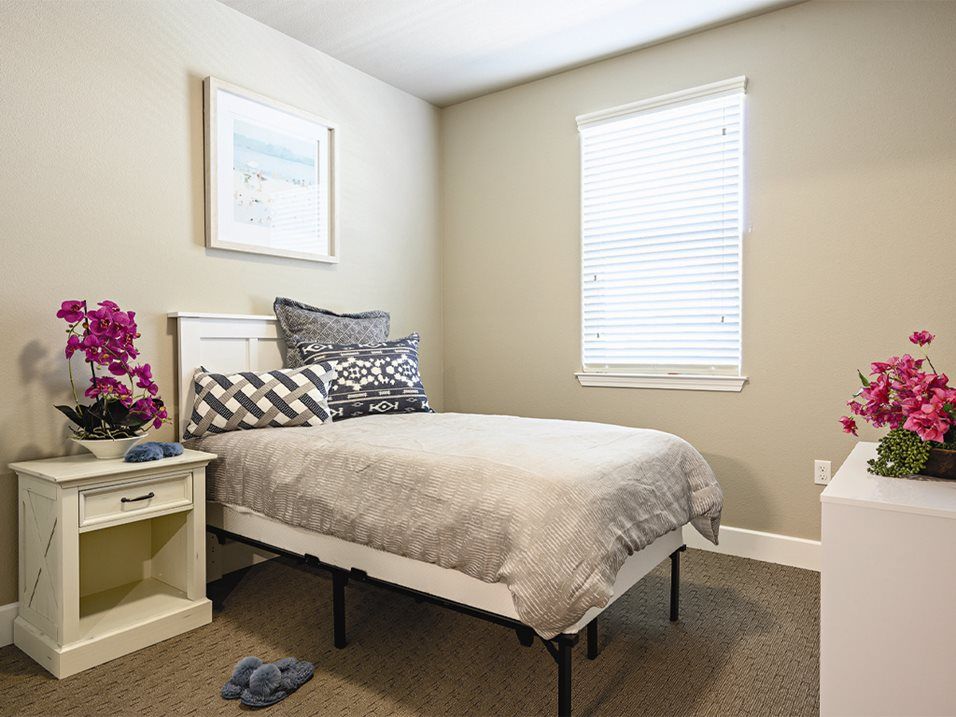 A neatly arranged bedroom with a single bed, a nightstand, and a window.