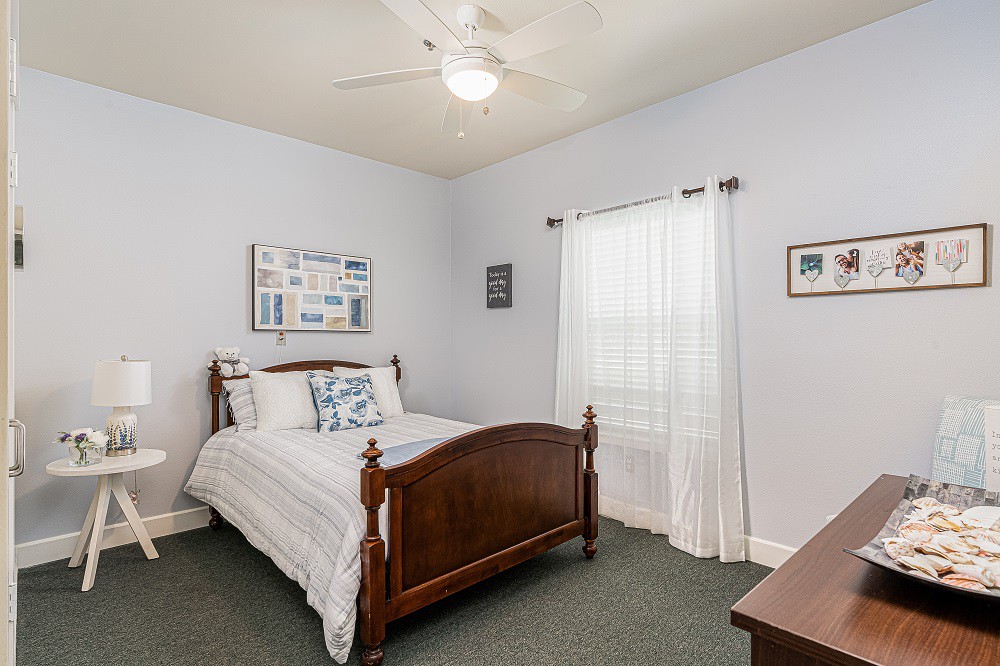 A cozy bedroom with a wooden bed, white bedding, and a ceiling fan.