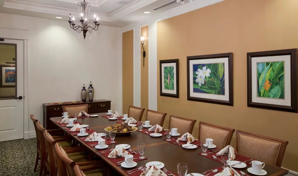 A formal dining room set up for a meeting or dinner, featuring a long table with neatly arranged place settings and elegant decor.