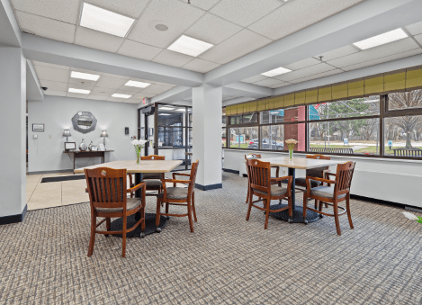 A bright and spacious cafeteria with wooden tables and chairs, featuring large windows.