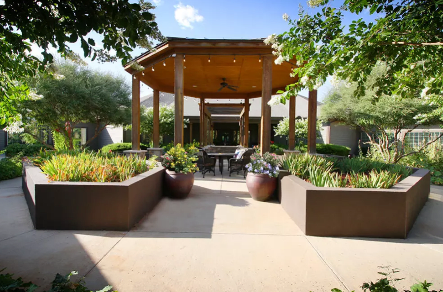 A beautifully landscaped patio with a wooden gazebo and outdoor seating surrounded by lush plants.