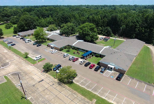 Aerial view of a commercial complex surrounded by trees and featuring an organized parking lot.
