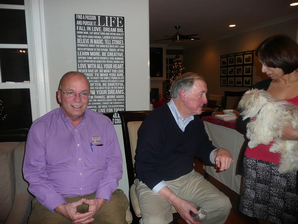 Two men seated indoors with a dog.