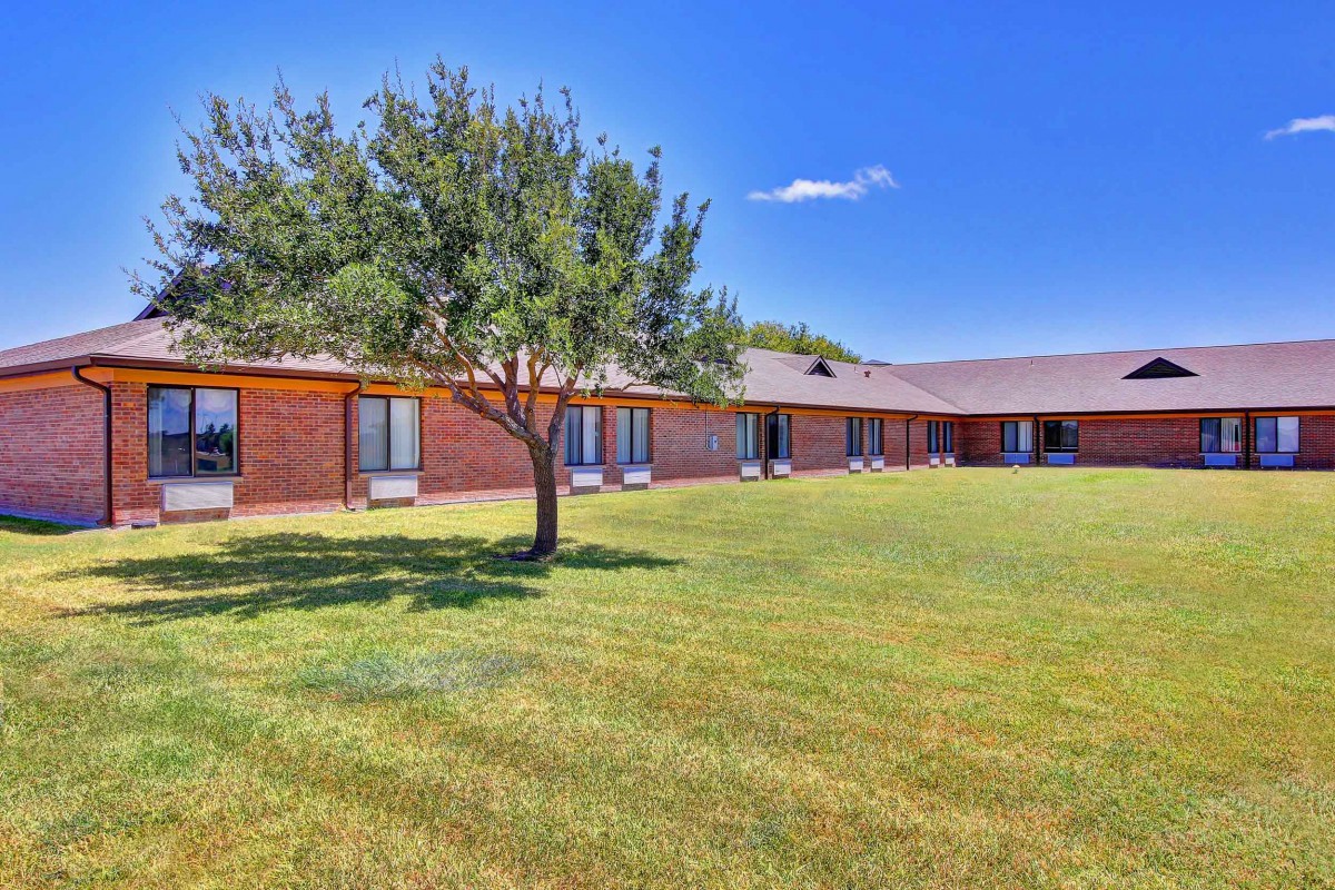 A brick building with a tree and expansive lawn under a clear blue sky.