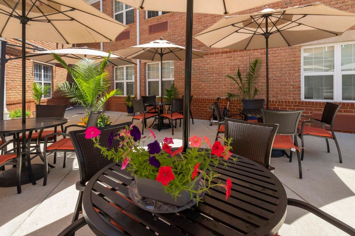 A cozy outdoor patio with tables, chairs, and colorful flowers under large umbrellas.