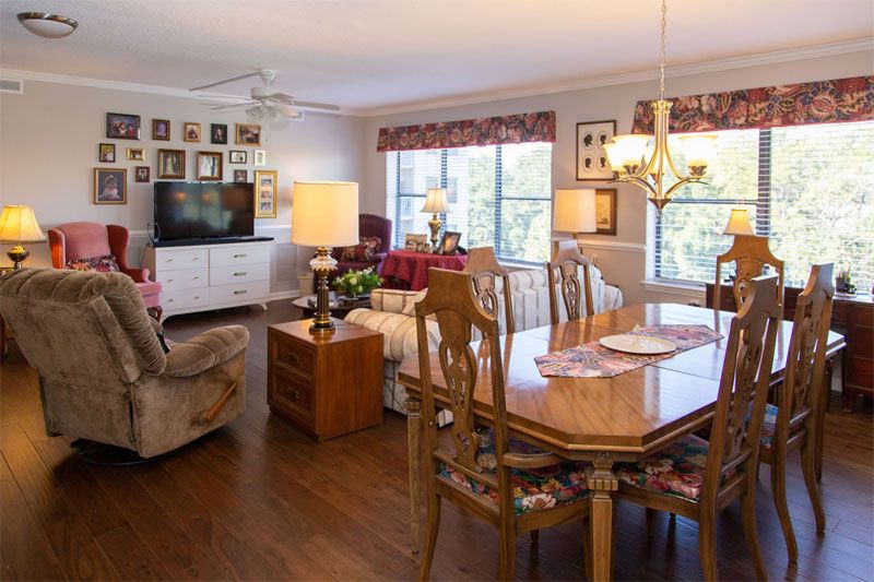 A cozy living and dining area with wooden flooring, featuring a dining table, comfortable seating, a television, and large windows allowing natural light.