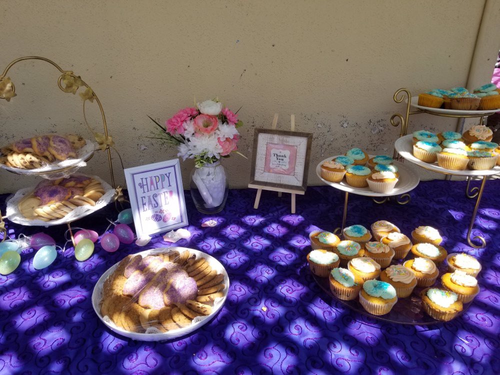A beautifully arranged dessert table featuring cupcakes and pastries on a purple tablecloth, adorned with flowers and framed signs.