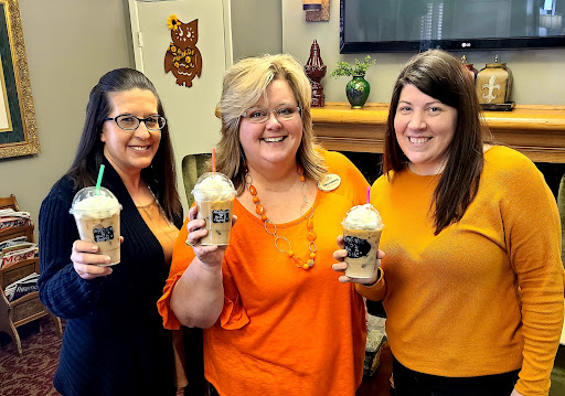 Three friends enjoying iced drinks, all dressed in orange, celebrating together.