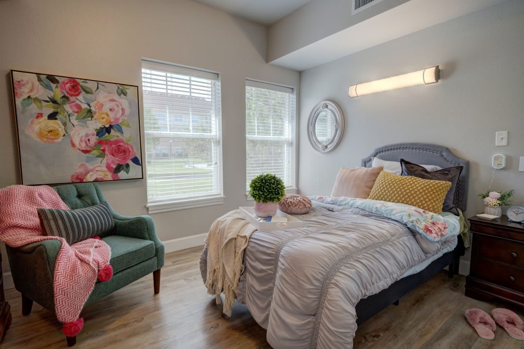A cozy and modern bedroom with a neatly made bed, floral artwork, and an upholstered chair.