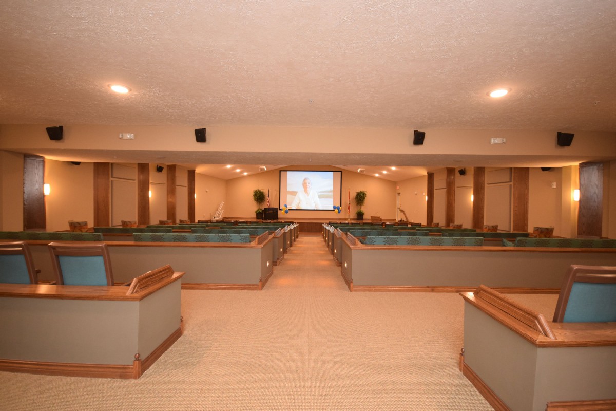 A church interior with rows of pews and a central aisle leading to a baptismal font and projector screen.