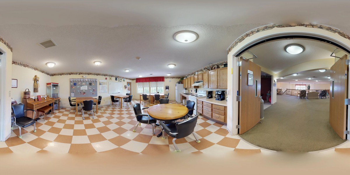 A spacious kitchen and dining area with wooden cabinets, a round table, and chairs set on a checkered tile floor.