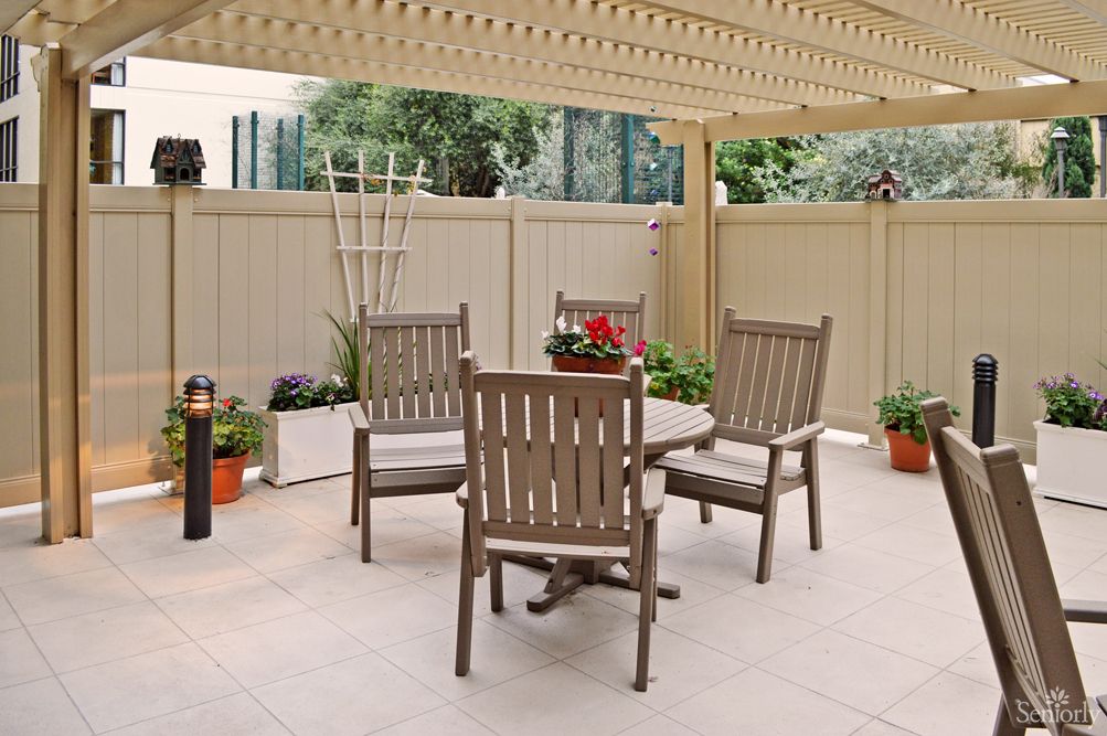 A cozy outdoor patio with wooden furniture and potted plants under a pergola.