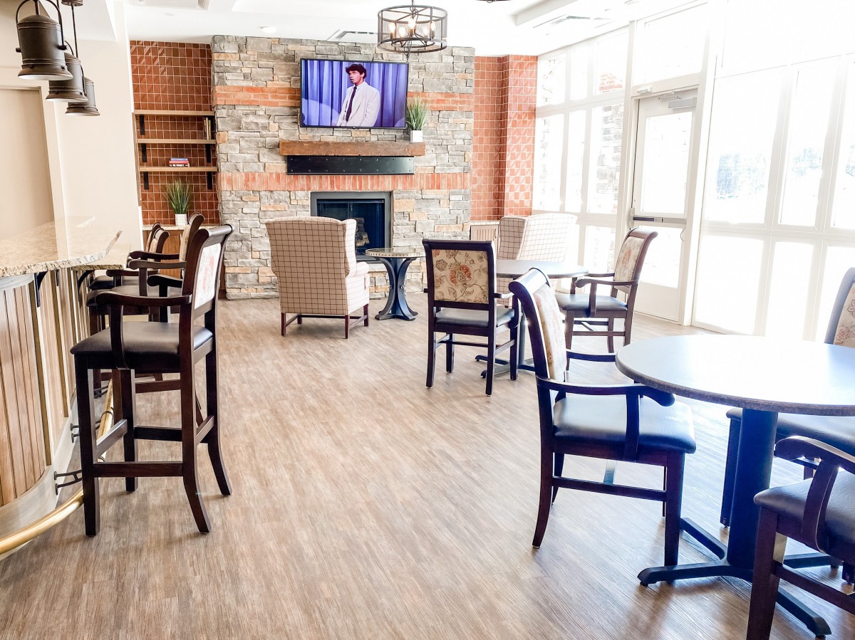 A cozy lounge area with chairs and tables, featuring a fireplace and a television mounted above.
