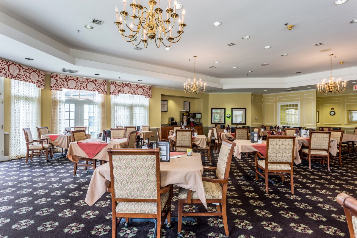 A spacious dining room with neatly arranged tables and chairs under elegant chandeliers.