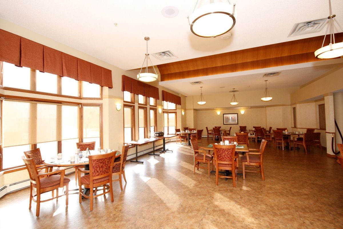 A spacious dining hall with large windows, wooden tables and chairs, and ceiling lights.
