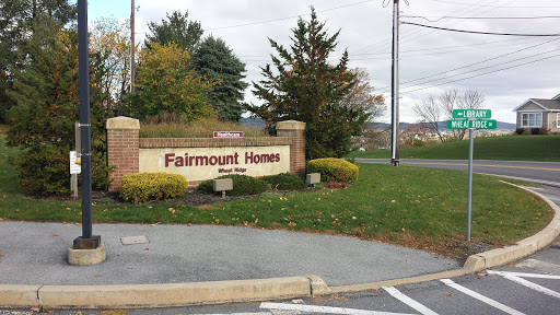 Entrance sign for Fairmount Homes surrounded by greenery and a cloudy sky.