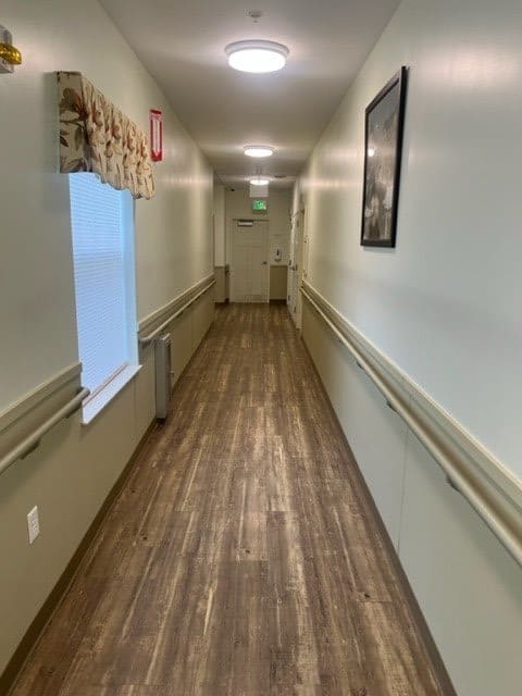 A long hallway with a wooden floor, featuring a window and wall decorations.
