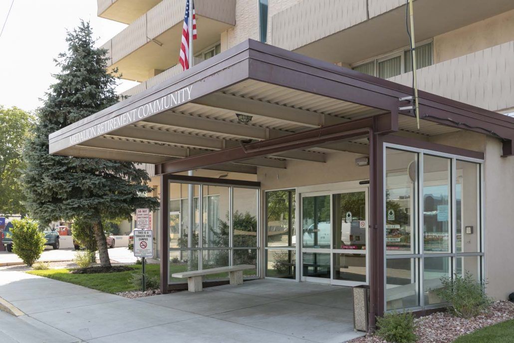 Entrance of a modern building with a glass canopy and an American flag.