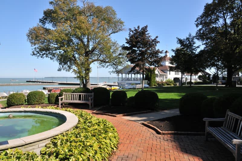 A scenic garden with a brick pathway, surrounded by trees and a view of the lake.