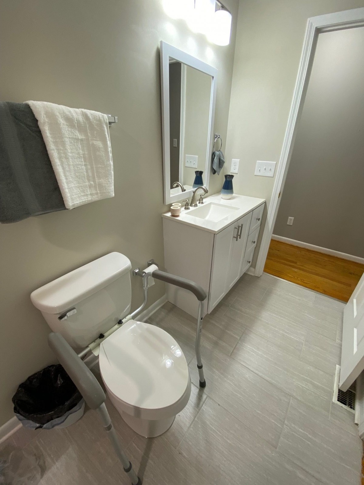 A modern bathroom featuring a toilet with a grab bar, a sink with a large mirror, and neatly arranged towels.