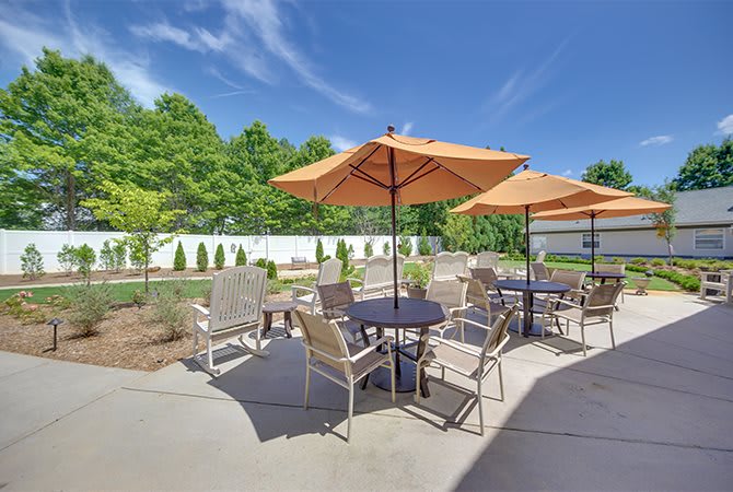 An outdoor patio with tables, chairs, and sun umbrellas under a clear blue sky.