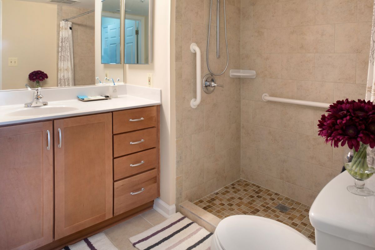 A bathroom featuring a walk-in shower with grab bars, a wooden vanity with drawers, and a mirror above the sink.