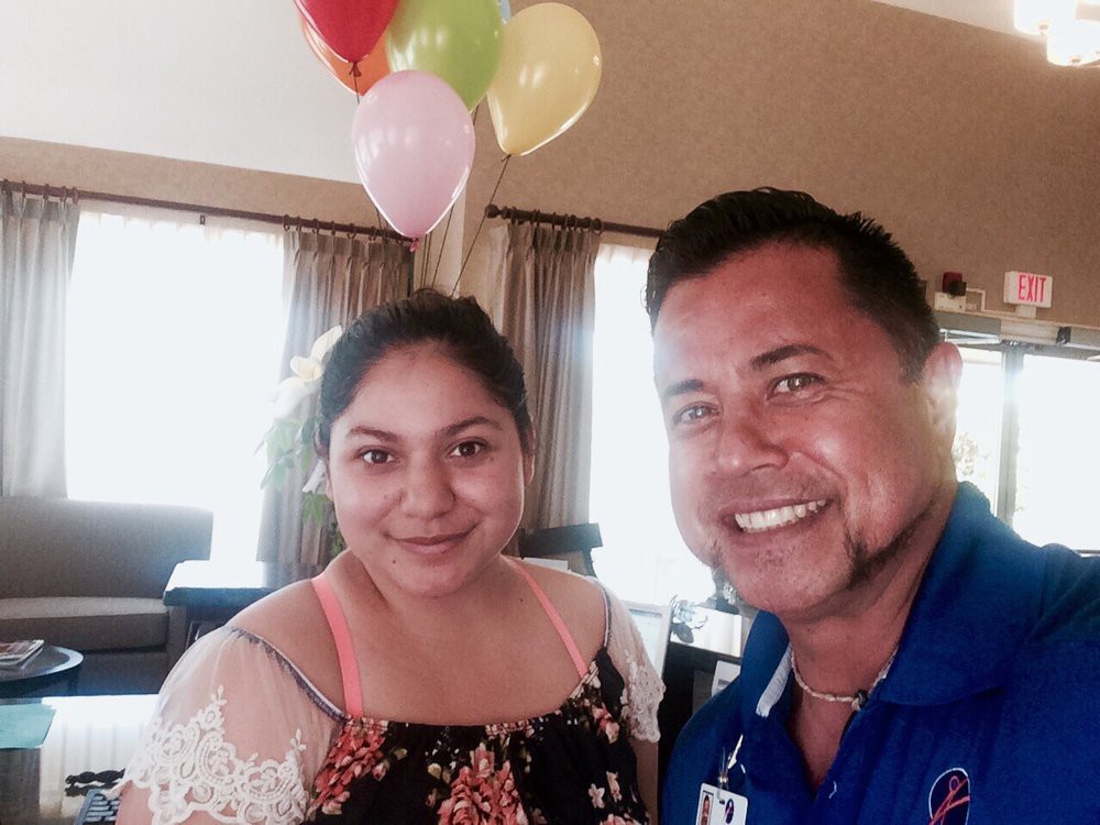 Two people smiling indoors with balloons in the background.