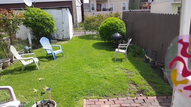 A backyard featuring a well-maintained lawn with chairs, a small grill, and a garden shed.