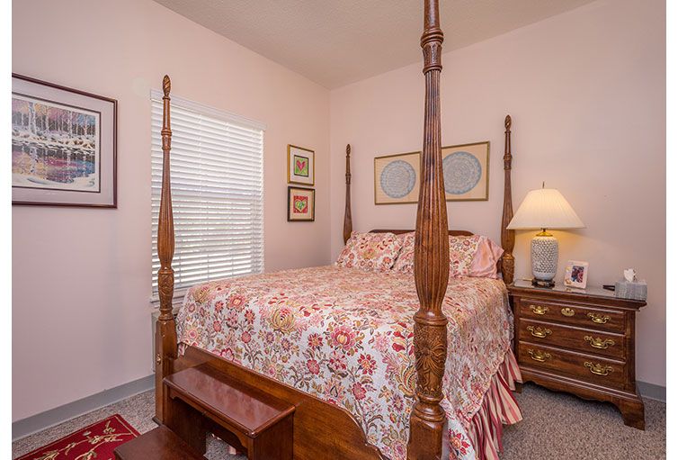 A cozy bedroom featuring a four-poster bed with decorative bedding, complemented by a nightstand with a lamp and framed artwork on the walls.