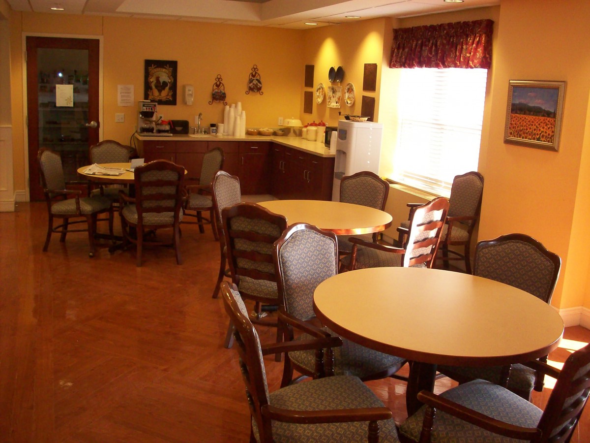 A cozy dining room with several tables and chairs, featuring a kitchen area in the background.