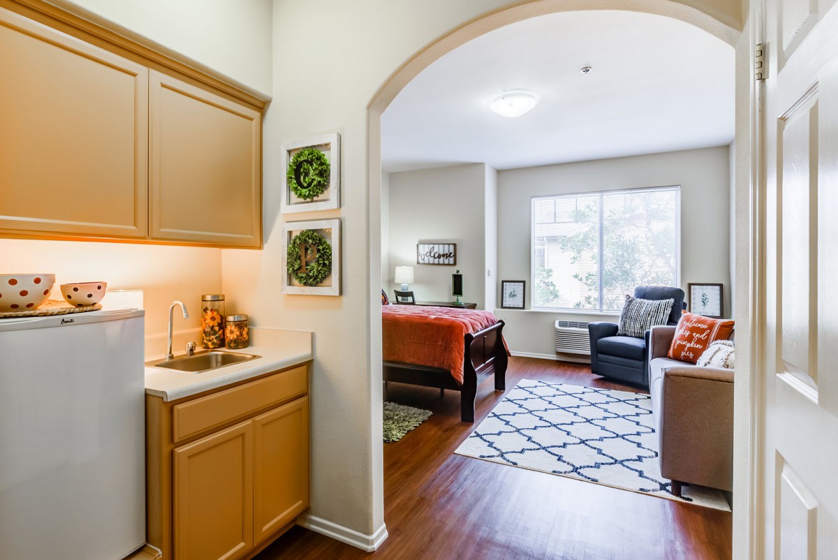 A cozy apartment interior featuring a kitchenette and a bedroom area with ample natural light.