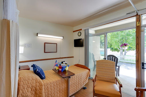 A bright and comfortable hospital room featuring two beds, a seating area, and access to an outdoor space.