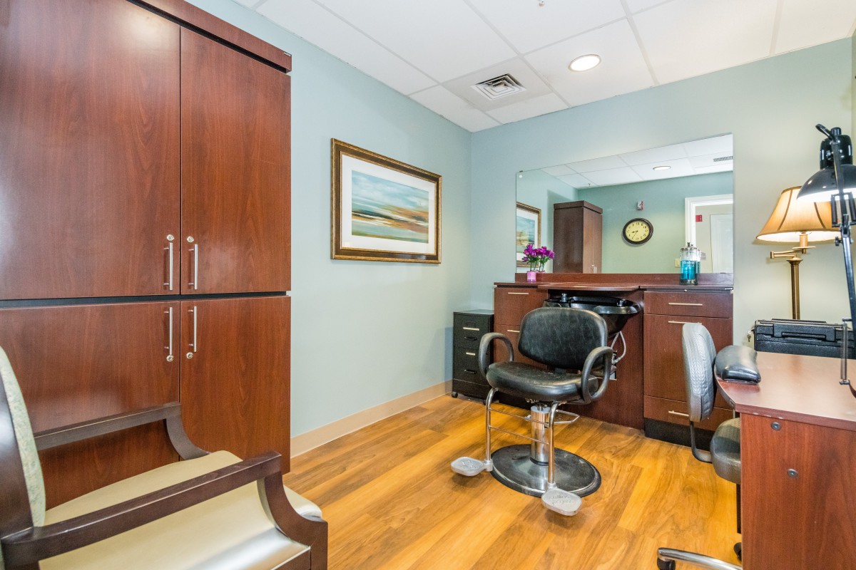 A modern salon interior with a styling chair and mirror, featuring wooden furniture and flooring.