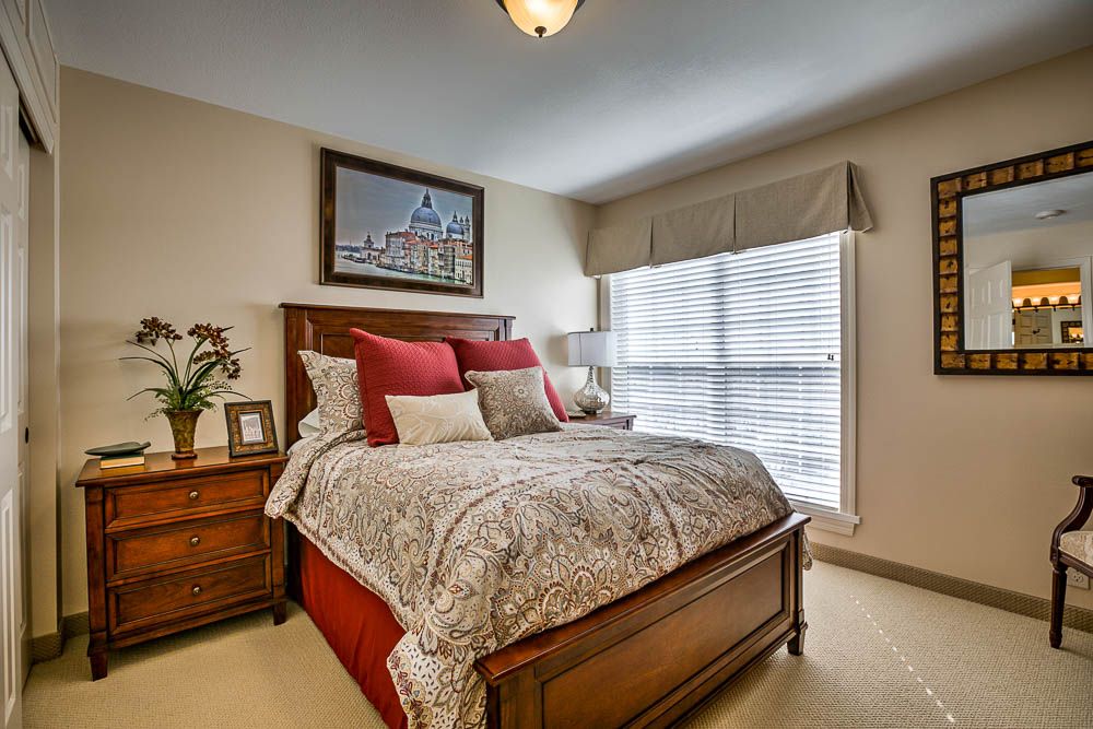 A cozy bedroom featuring a large bed with red and gray bedding, a bedside table with decor, and a picture hanging above the bed.