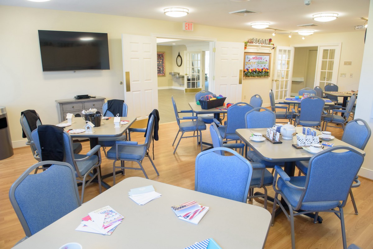 A communal dining area with tables and chairs, featuring a wall-mounted television.