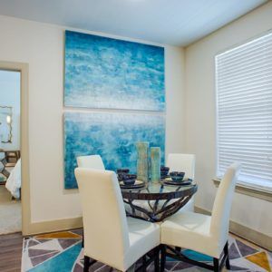 A modern dining room with a round table and white chairs, featuring abstract blue artwork on the wall.