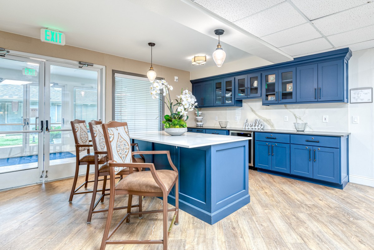 A modern kitchen with blue cabinets and a central island, featuring wooden bar stools and pendant lighting.