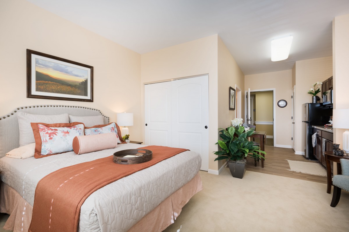 A modern bedroom with a neatly made bed, artwork on the wall, and decorative plants.