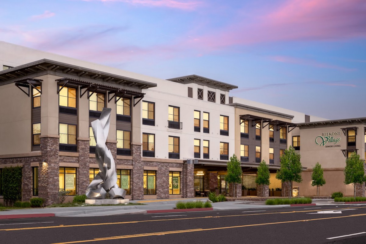 A modern building with a prominent statue in front, set against a colorful sky.