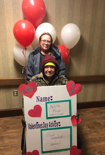 Two friends celebrating Valentine's Day with balloons and a fun sign.
