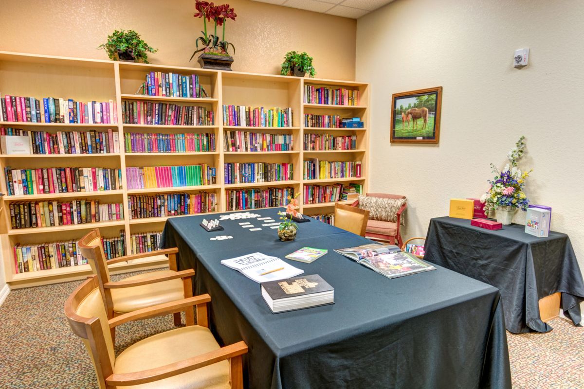 A cozy library with shelves of colorful books, a table with chairs for meetings or reading, and decorative plants.