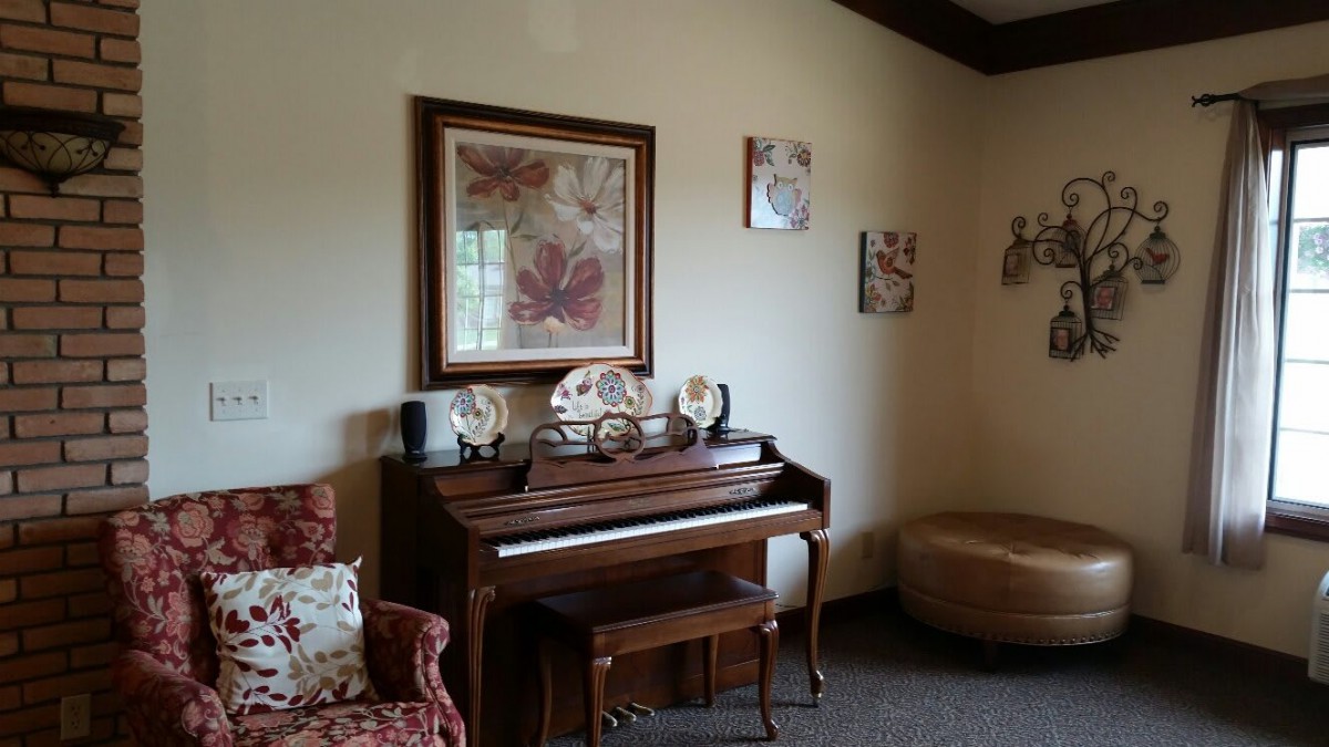 A cozy living room with a wooden piano surrounded by decorative artwork and furniture.