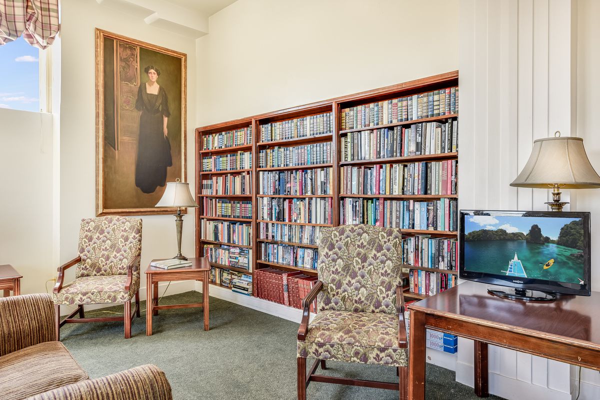 A cozy library corner with bookshelves, a portrait, and comfortable chairs.