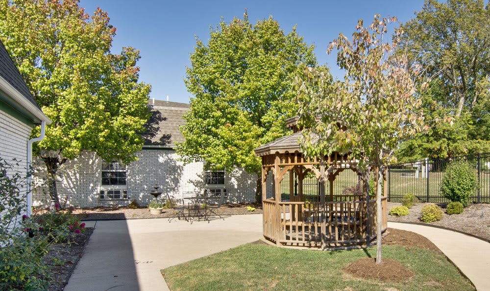 A peaceful outdoor scene featuring a wooden gazebo surrounded by trees and a building.
