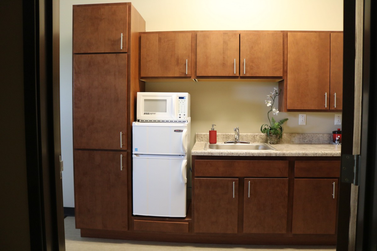 A compact kitchen setup featuring wooden cabinets, a microwave, refrigerator, and sink.